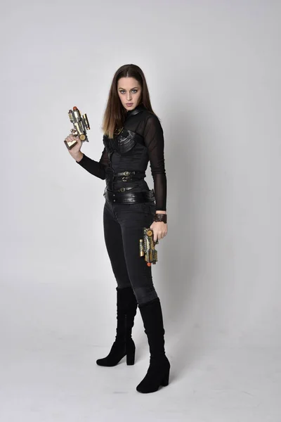 全长肖像一个漂亮的黑发女人穿着黑色皮革幻想服装与枪 站在工作室背景上的姿势 — 图库照片