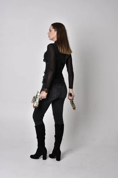 全长肖像一个漂亮的黑发女人穿着黑色皮革幻想服装与枪 站在工作室背景上的姿势 — 图库照片