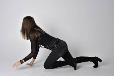 Siyah deri fantezi kostüm giyen güzel esmer bir kadının tam boy portresi. Stüdyo geçmişiyle oturuyor..