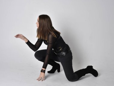 Siyah deri fantezi kostüm giyen güzel esmer bir kadının tam boy portresi. Stüdyo geçmişiyle oturuyor..