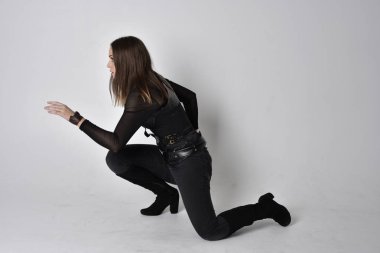 Siyah deri fantezi kostüm giyen güzel esmer bir kadının tam boy portresi. Stüdyo geçmişiyle oturuyor..