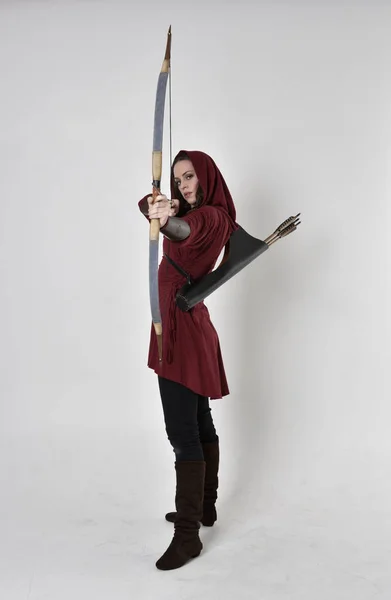 一个黑发女孩的全长肖像 身穿红色幻想服 头戴头巾 手持弓箭 站在白色工作室背景上的姿势 — 图库照片