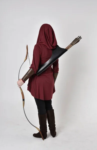 一个黑发女孩的全长肖像 身穿红色幻想服 头戴头巾 手持弓箭 站在白色工作室背景上的姿势 — 图库照片