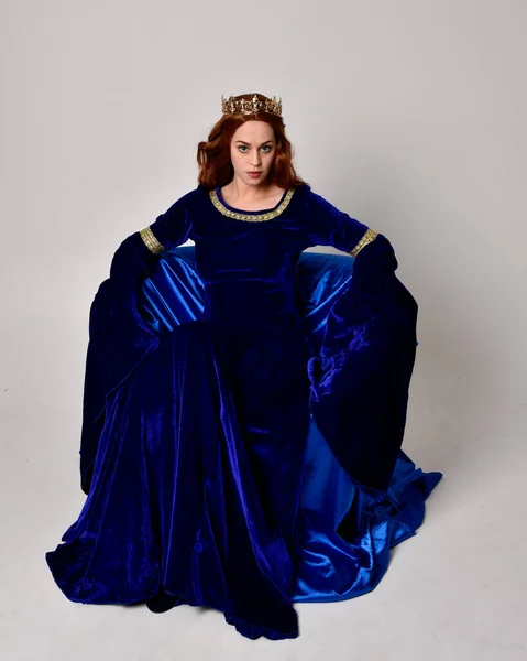 파란색 가운을 왕관을 소녀의 전체긴 초상화 스튜디오 배경에 자세로 앉아서 — 스톡 사진