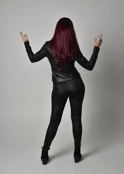 身穿黑色皮夹克 裤子和靴子的红头发女孩的全长肖像 站立姿势 面对着相机 与灰色的工作室背景隔离 — 图库照片
