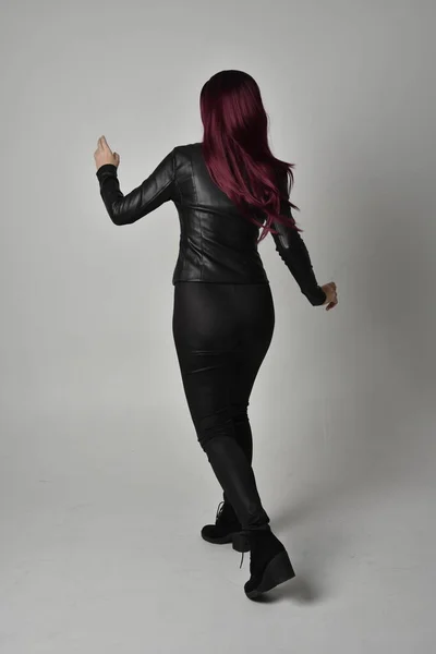 身穿黑色皮夹克 裤子和靴子的红头发女孩的全长肖像 站立姿势 面对着相机 与灰色的工作室背景隔离 — 图库照片
