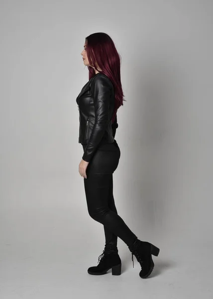 身穿黑色皮夹克 裤子和靴子的红头发女孩的全长肖像 站在侧面的姿态 与灰色的工作室背景隔离 — 图库照片