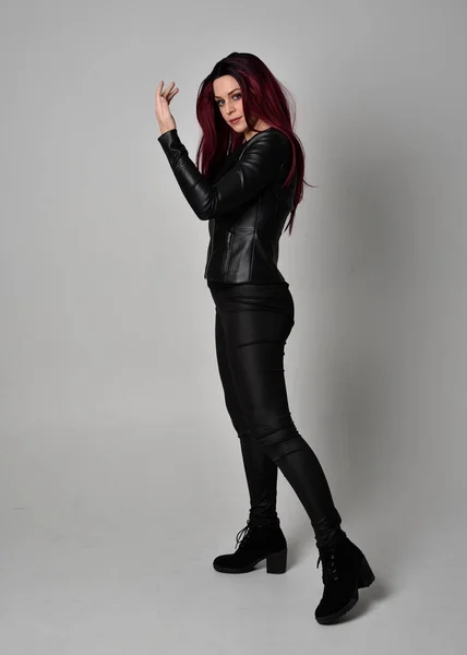 身穿黑色皮夹克 裤子和靴子的红头发女孩的全长肖像 站在侧面的姿态 与灰色的工作室背景隔离 — 图库照片