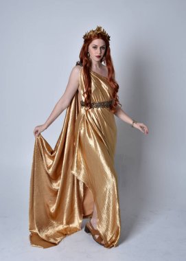 Full length portrait of girl with red hair wearing long grecian toga and golden wreath. Standing pose iisolated against a grey studio background. clipart