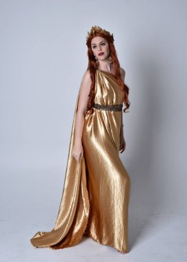 Kızıl saçlı, uzun Yunan togası ve altın çelenk giyen bir kızın tam boy portresi. Gri bir stüdyonun arka planında izole bir şekilde duruyor..