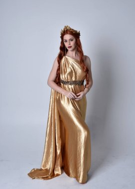 Kızıl saçlı, uzun Yunan togası ve altın çelenk giyen bir kızın tam boy portresi. Gri bir stüdyonun arka planında izole bir şekilde duruyor..