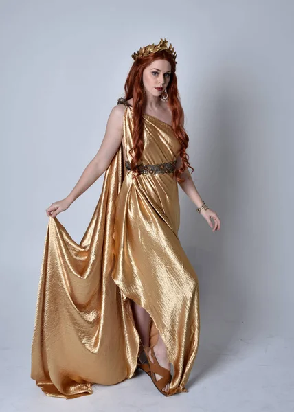 Kızıl saçlı, uzun Yunan togası ve altın çelenk giyen bir kızın tam boy portresi. Gri bir stüdyonun arka planında izole bir şekilde duruyor..