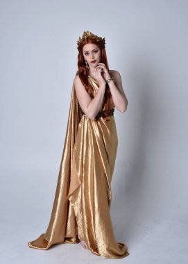 Kızıl saçlı, uzun Yunan togası ve altın çelenk giyen bir kızın tam boy portresi. Gri bir stüdyonun arka planında izole bir şekilde duruyor..