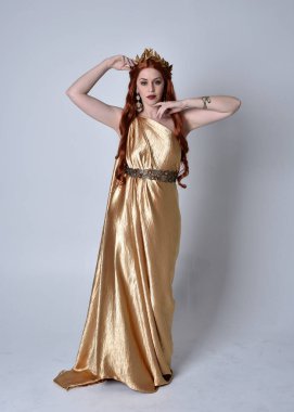 Kızıl saçlı, uzun Yunan togası ve altın çelenk giyen bir kızın tam boy portresi. Gri bir stüdyonun arka planında izole bir şekilde duruyor..