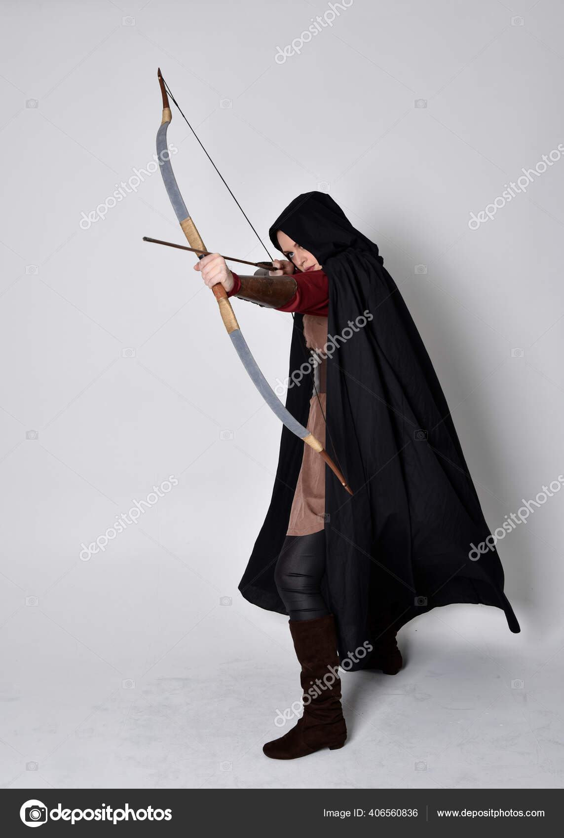 黒のマントで中世の射手の衣装を身に着けている赤い髪の少女の完全な長