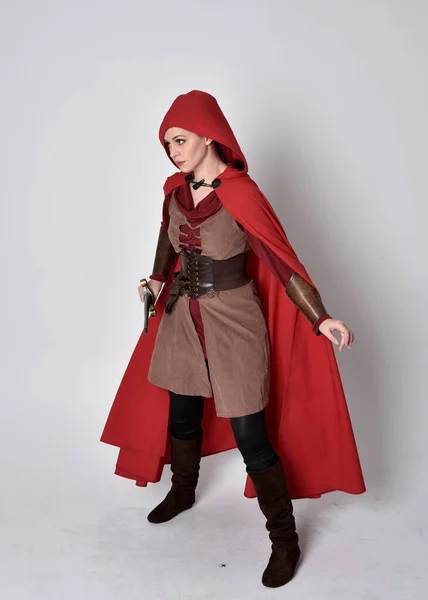 穿着中世纪服装和红色斗篷的女孩的全长肖像 拿着剑站在那里 与灰色的工作室背景隔离 — 图库照片