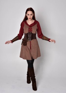 Ortaçağ kostümü giymiş bir kızın tam boy portresi. Gri bir stüdyonun arka planında, elinde kılıçla dikiliyordu..