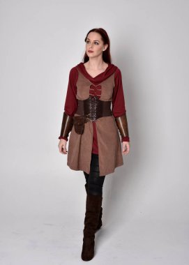 Ortaçağ kostümü giymiş bir kızın tam boy portresi. Gri bir stüdyonun arka planında, elinde kılıçla dikiliyordu..