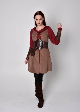 Ortaçağ kostümü giymiş bir kızın tam boy portresi. Gri bir stüdyonun arka planında, elinde kılıçla dikiliyordu..