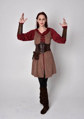 Ortaçağ kostümü giymiş bir kızın tam boy portresi. Gri bir stüdyonun arka planında, elinde kılıçla dikiliyordu..