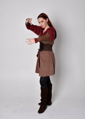 Ortaçağ kostümü giymiş bir kızın tam boy portresi. Gri bir stüdyonun arka planında, elinde kılıçla dikiliyordu..