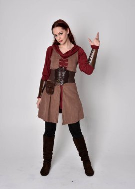 Ortaçağ kostümü giymiş bir kızın tam boy portresi. Gri bir stüdyonun arka planında, elinde kılıçla dikiliyordu..