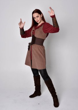 Ortaçağ kostümü giymiş bir kızın tam boy portresi. Gri bir stüdyonun arka planında, elinde kılıçla dikiliyordu..