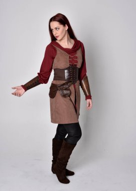 Ortaçağ kostümü giymiş bir kızın tam boy portresi. Gri bir stüdyonun arka planında, elinde kılıçla dikiliyordu..