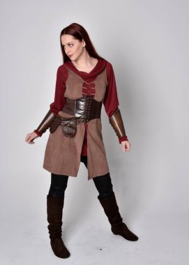 Ortaçağ kostümü giymiş bir kızın tam boy portresi. Gri bir stüdyonun arka planında, elinde kılıçla dikiliyordu..