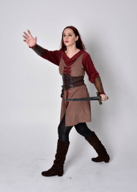 Ortaçağ kostümü giymiş bir kızın tam boy portresi. Gri bir stüdyonun arka planında, elinde kılıçla dikiliyordu..