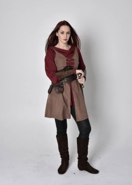 Ortaçağ kostümü giymiş bir kızın tam boy portresi. Gri bir stüdyonun arka planında, elinde kılıçla dikiliyordu..