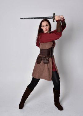 Ortaçağ kostümü giymiş bir kızın tam boy portresi. Gri bir stüdyonun arka planında, elinde kılıçla dikiliyordu..