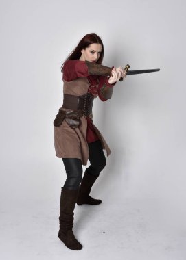 Ortaçağ kostümü giymiş bir kızın tam boy portresi. Gri bir stüdyonun arka planında, elinde kılıçla dikiliyordu..