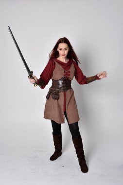 Ortaçağ kostümü giymiş bir kızın tam boy portresi. Gri bir stüdyonun arka planında, elinde kılıçla dikiliyordu..