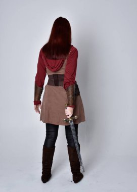 Ortaçağ kostümü giymiş bir kızın tam boy portresi. Elinde kılıçla kameraya dönük bir poz. Gri bir arka planda izole edilmiş..