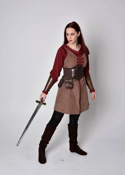 穿着中世纪服装的女孩的全长肖像 拿着剑站在那里 与灰色的工作室背景隔离 — 图库照片