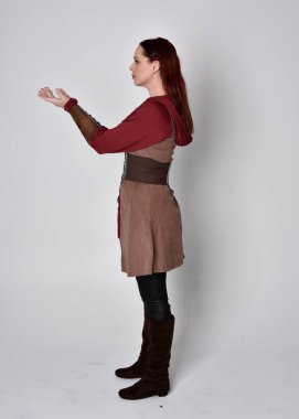 Ortaçağ kostümü giymiş bir kızın tam boy portresi. Gri bir stüdyonun arka planında, kameraya dönük poz veriyor..