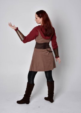 Ortaçağ kostümü giymiş bir kızın tam boy portresi. Gri bir stüdyonun arka planında, kameraya dönük poz veriyor..