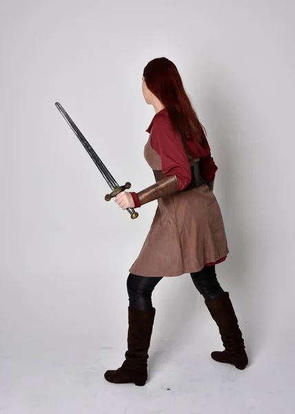 中世の衣装を着た少女の完全な長さの肖像画 灰色のスタジオの背景に隔離されたカメラに背を向けて剣を保持立ちポーズ — ストック写真