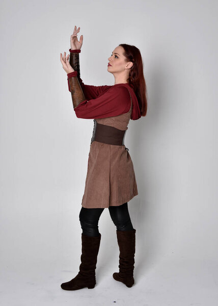 Full length portrait of girl wearing medieval costume. Standing pose with back to the camera,  isolated against a grey studio background.