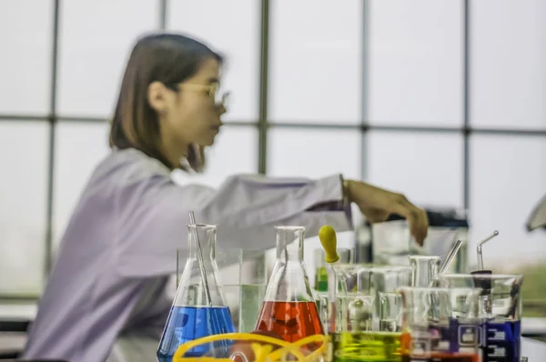 Sağlık renkli kimyasal şişeleri ve masanın üzerine yerleştirilen tüpler ile kimya laboratuarında çalışan kadın bilim adamı oturma Analizi ve iş ile meşgul. Kozmetik ve güzellik ürünleri hakkında.