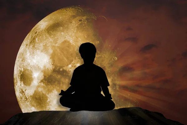 Silhouette of a man relaxing meditation in nature, on a sloping rocky cliff with a twilight sky background with a super moon beautiful , Elements of this image furnished by NASA