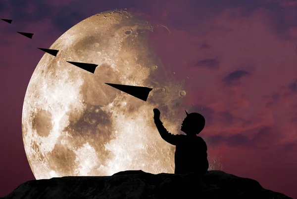 立って 喜んでミステリー スカイライン美しい月 Nasa から提供されたこのイメージの要素と急な岩の崖の空気で紙飛行機を投げる少年のシルエット — ストック写真