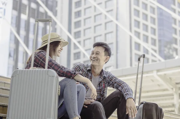 Young Asian Couple of travelers Smiling happily while sitting with a luggage, concept of traveling of lover of tourists south asian with background skyscraper