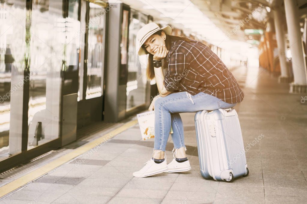 Asian women travelers, smile happily Hold the map in hand, Sit on your luggage for the sky train, With a happy gesture, concept of travel in summer.