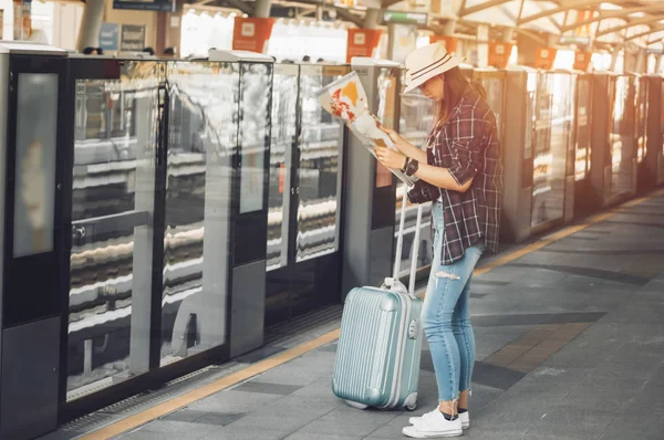 Beautiful woman travelers are checking their travel route with a map in hand and luggage, With concept of leisure, adventure and travel planner by train,During the summer holidays by yourself.