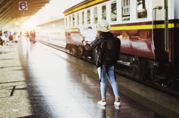 Blurred - Asian woman travelers with backpacking, see map in the railway station, planning a tour, with train parked in station, concept Travel Planning Alone.