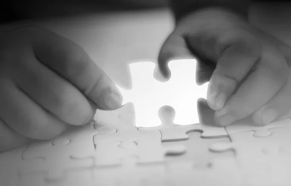 Two hands holding jigsaw puzzle piece glowing white glow piece missing from the components, Abstract concept of business with success and goals and corporate strategy, black and white tone