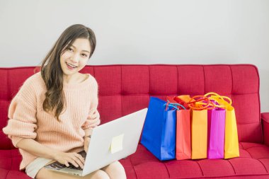 Güzel kadın kırmızı Kanepede oturan, renkli kağıt alışveriş çantası