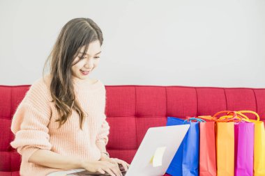 Güzel kadın kırmızı Kanepede oturan, renkli kağıt alışveriş çantası